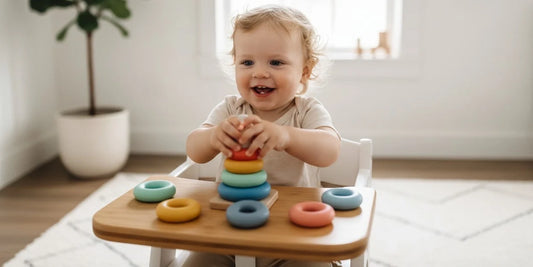 Smiling toddler playing with colorful stacking rings and shape sorter toys on a soft play mat